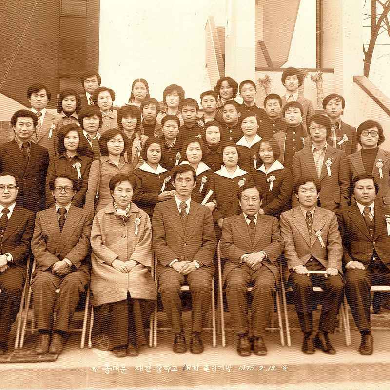 재건중학교 졸업기념 단체사진. 교복 입은 학생들과 교사진이 건물 계단에 모여 있다.